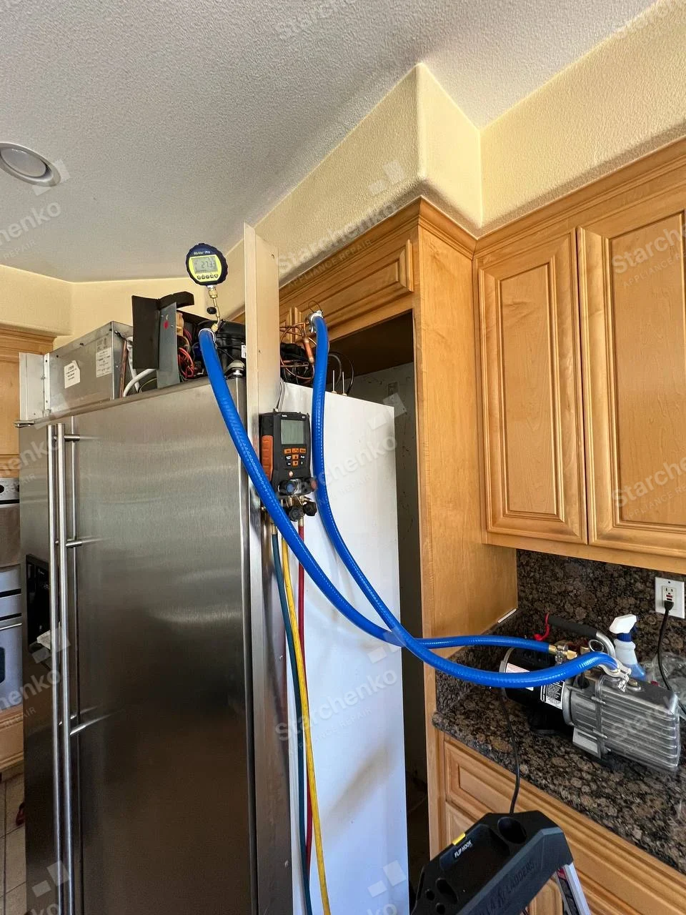 GE Profile repair: Stainless built-in refrigerator with top mechanical bay open and blue service hoses attached.
