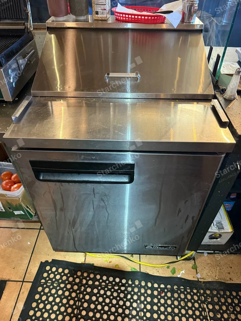 Everest repair: Commercial stainless refrigerated preparation cabinet with hinged top lid and front access door in restaurant kitchen.