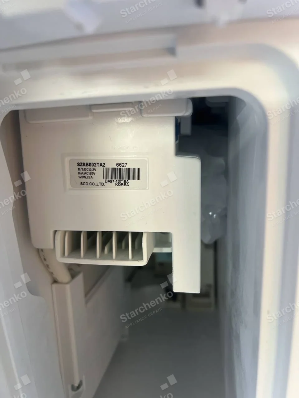Maytag repair: Close-up of internal refrigerator ice-maker module with ice visible behind it.
