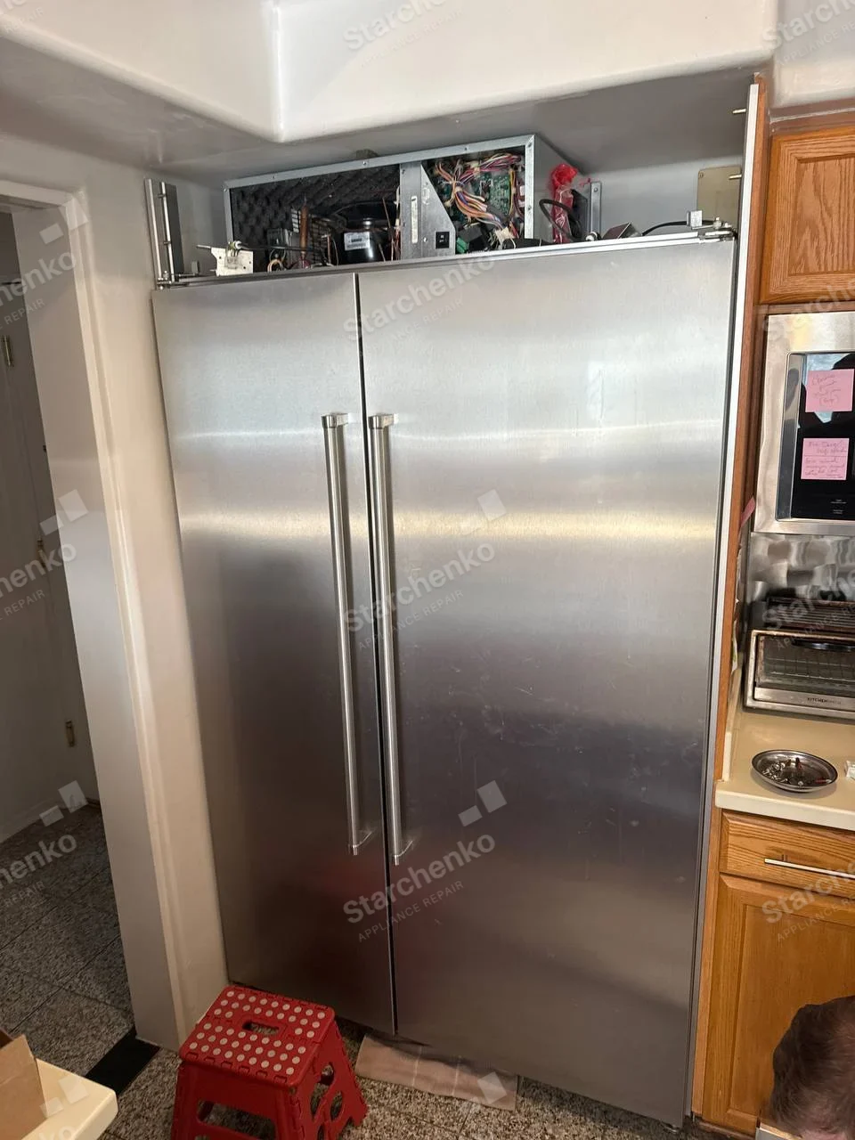 GE Profile repair: Built-in side-by-side refrigerator upper electronics and compressor area exposed.