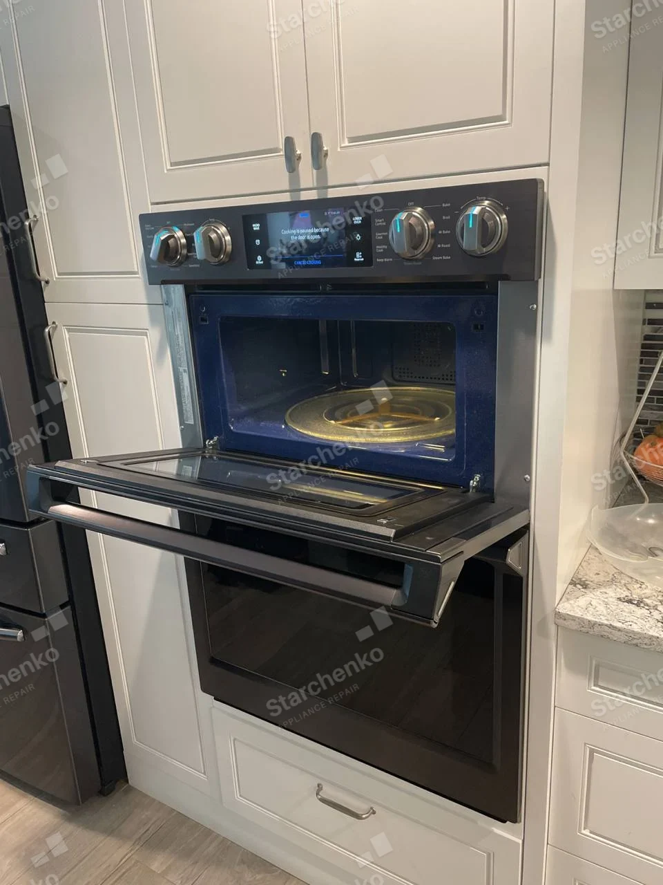 Samsung repair: Open built-in microwave with glass turntable above a separate wall oven, showing a paused-cooking message.