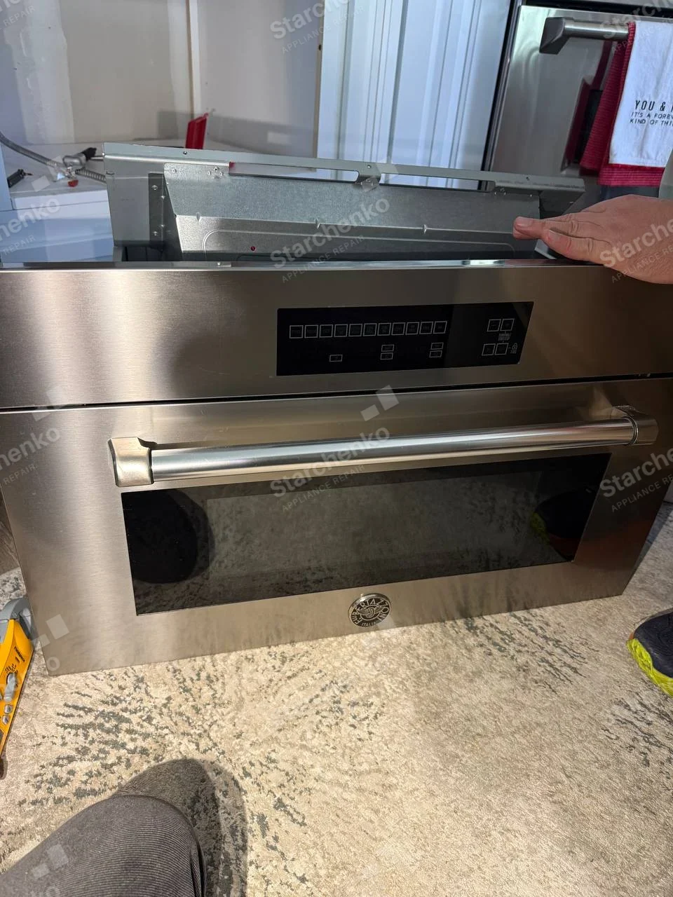 Built-in stainless oven removed from cabinet with top enclosure exposed, round Bertazzoni badge centered below door.