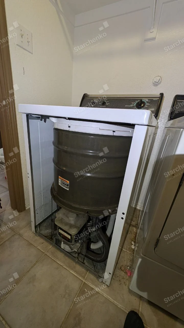 Amana repair: Top-load washer with front cabinet removed exposing wash tub, motor and drain hose.