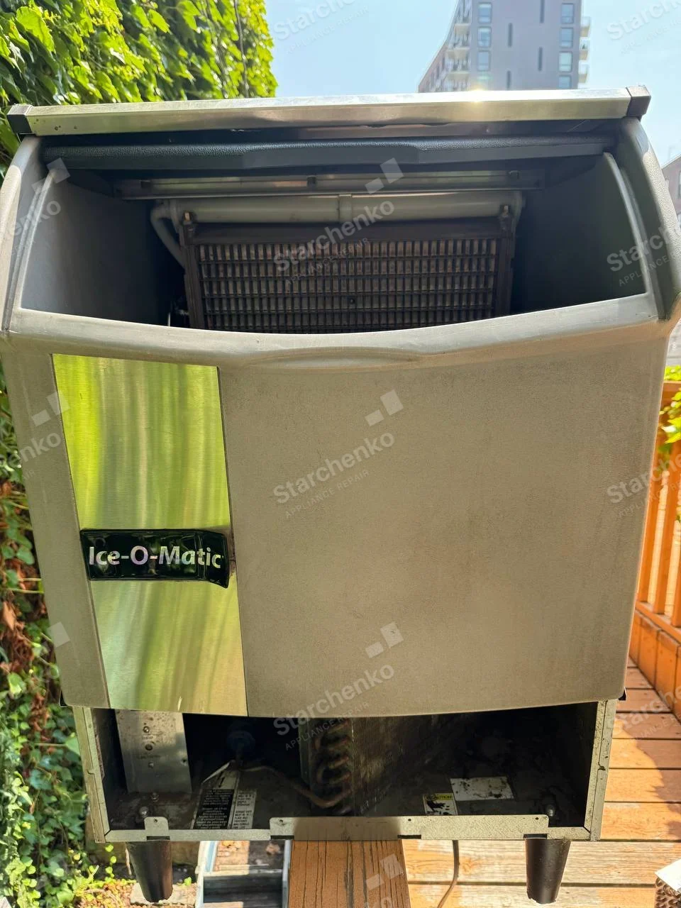Ice-O-Matic repair: Commercial ice-making machine head with front panel raised and lower compressor compartment open.