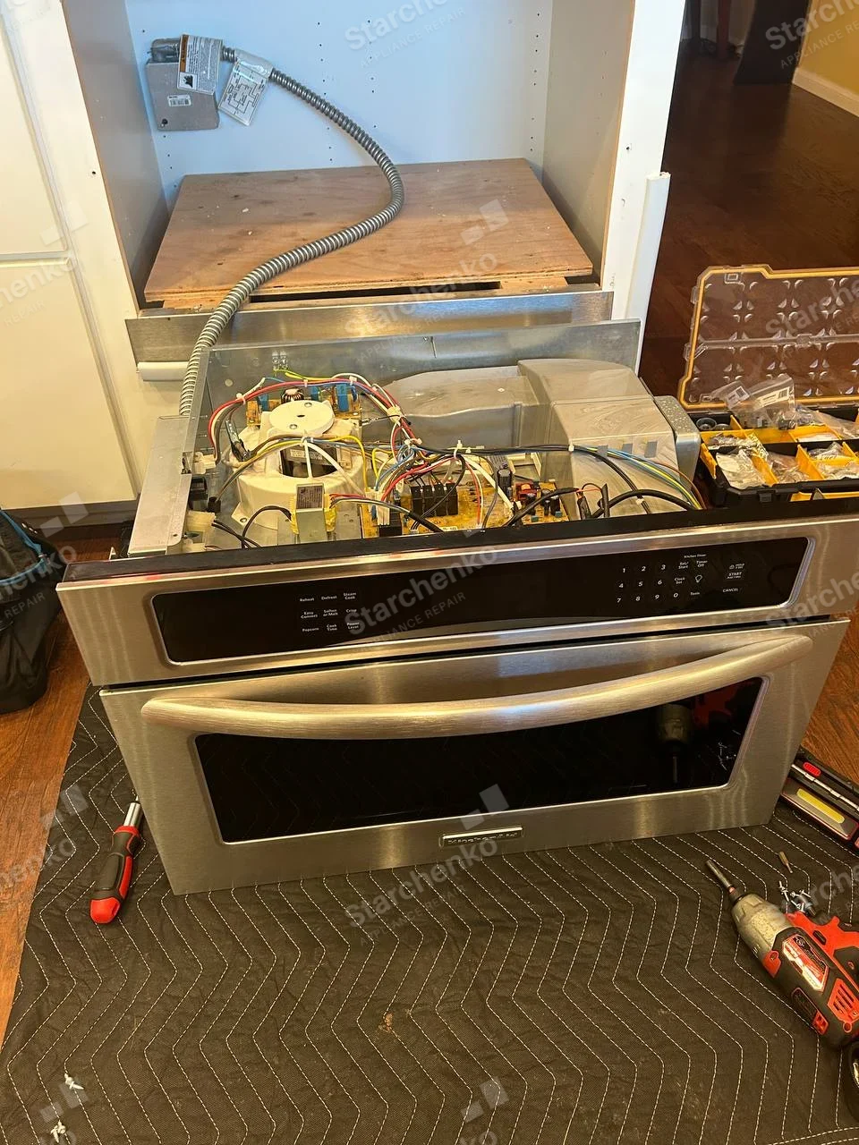 KitchenAid badge on lower center of oven door, upper control compartment open exposing wiring and boards.
