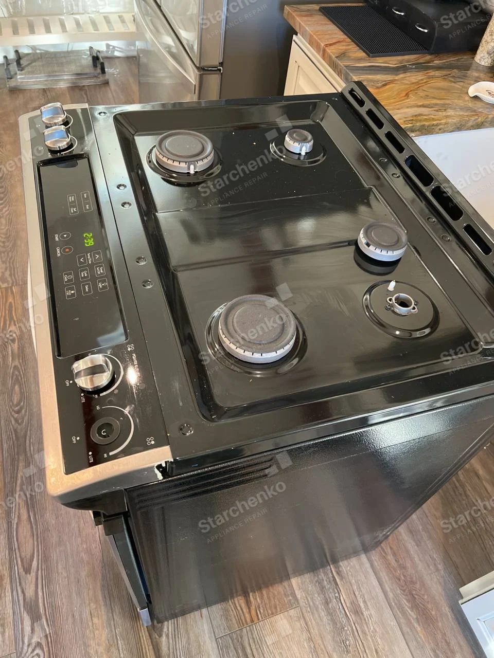 Amana repair: Black slide-in gas range pulled out with exposed burners and one missing burner cap.