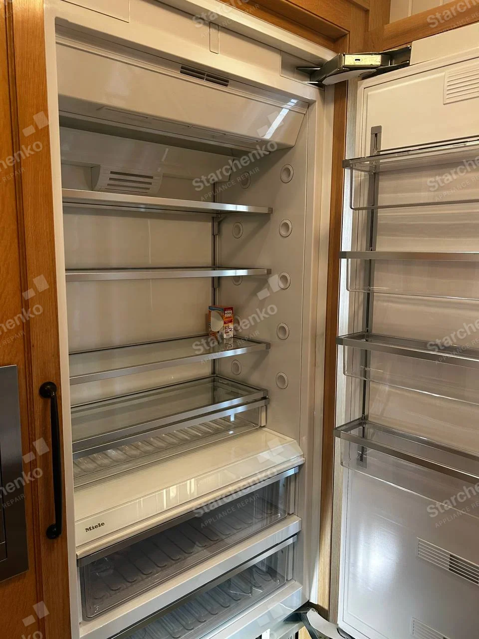 Miele integrated refrigerator with white interior, shelves and lower produce drawers, door open.