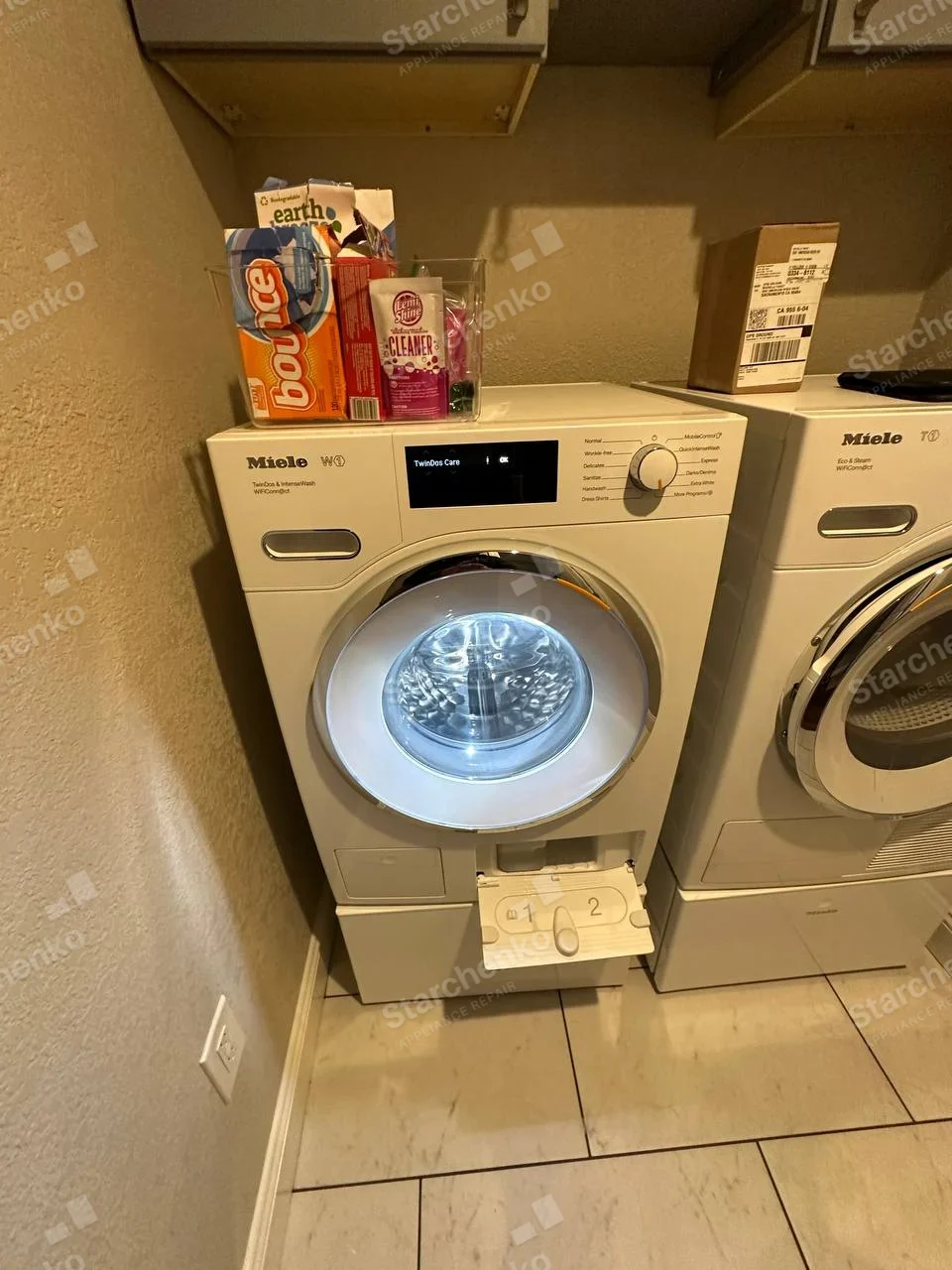 Miele W1 on main left front-load washer control fascia, small lower service flap open, matching right dryer separate.