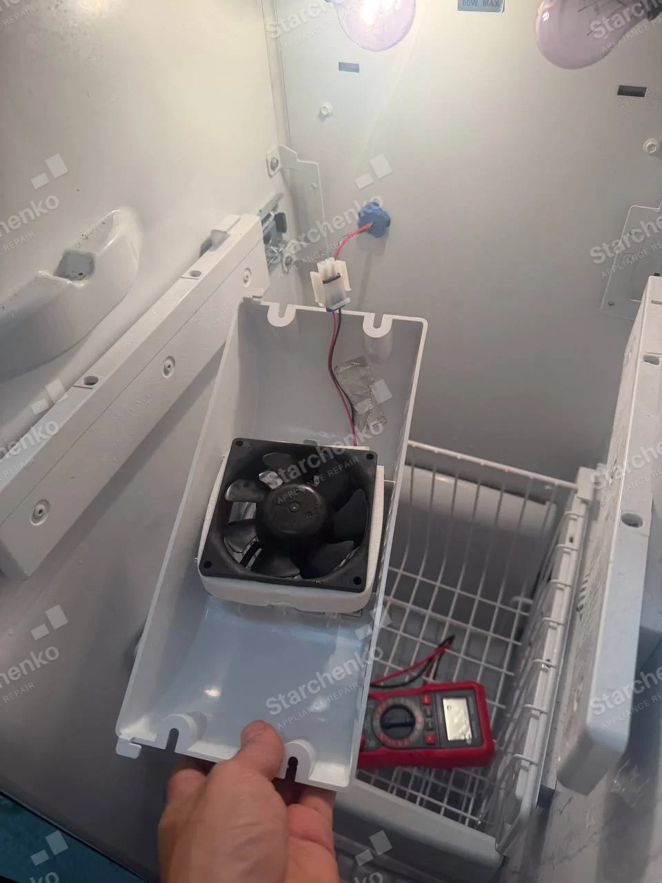 Freezer interior with detached evaporator-fan housing and multimeter, no maker mark visible.