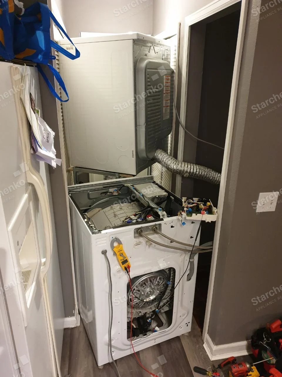 Frigidaire repair: Lower front-load washer below vented dryer, top and rear panels removed with motor and control electronics exposed.