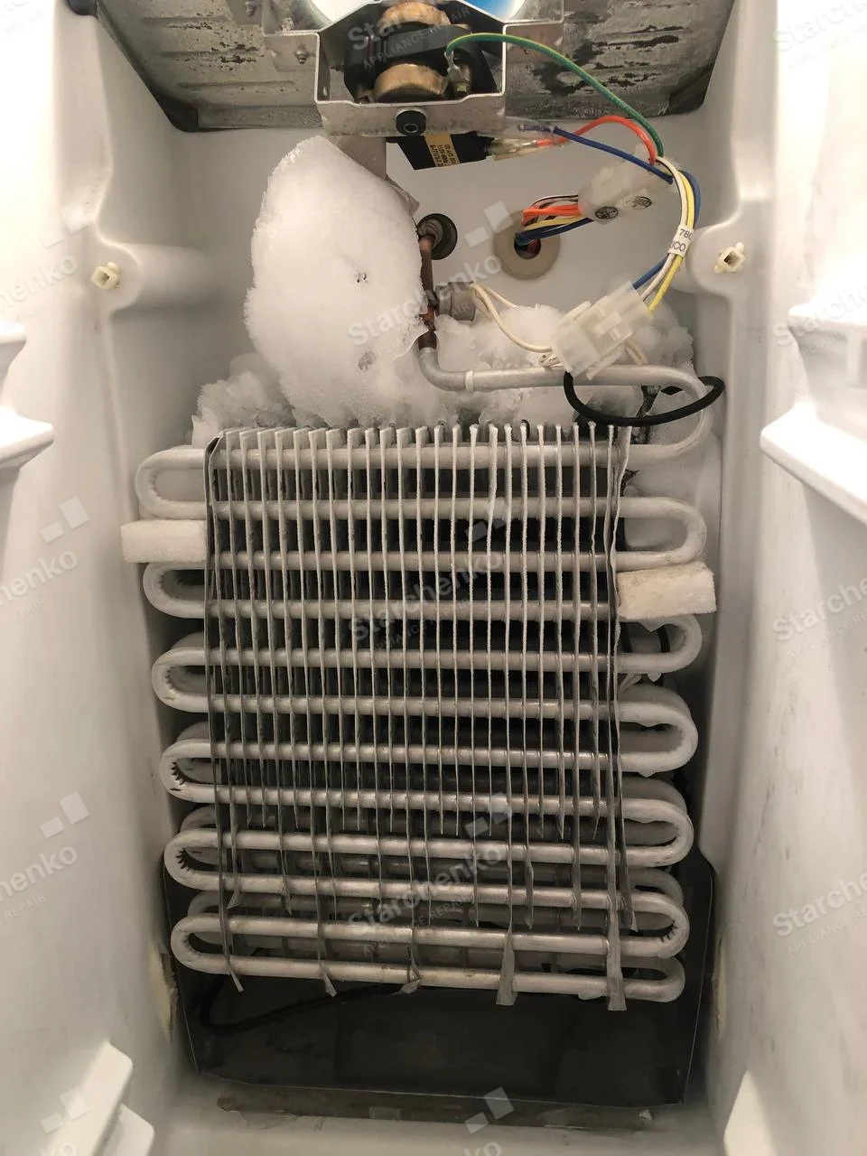 Maytag repair: Exposed refrigerator evaporator coil with large ice ball on upper tubing and fan above.