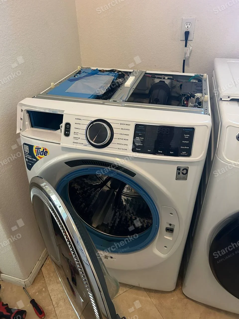 Frigidaire repair: Front-load washer with top cover removed and front door open, revealing drum and upper components, Tide is detergent promotion.
