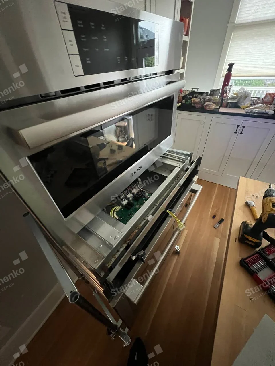 Bosch microwave and wall oven combination with the oven control panel lowered, exposing the control board