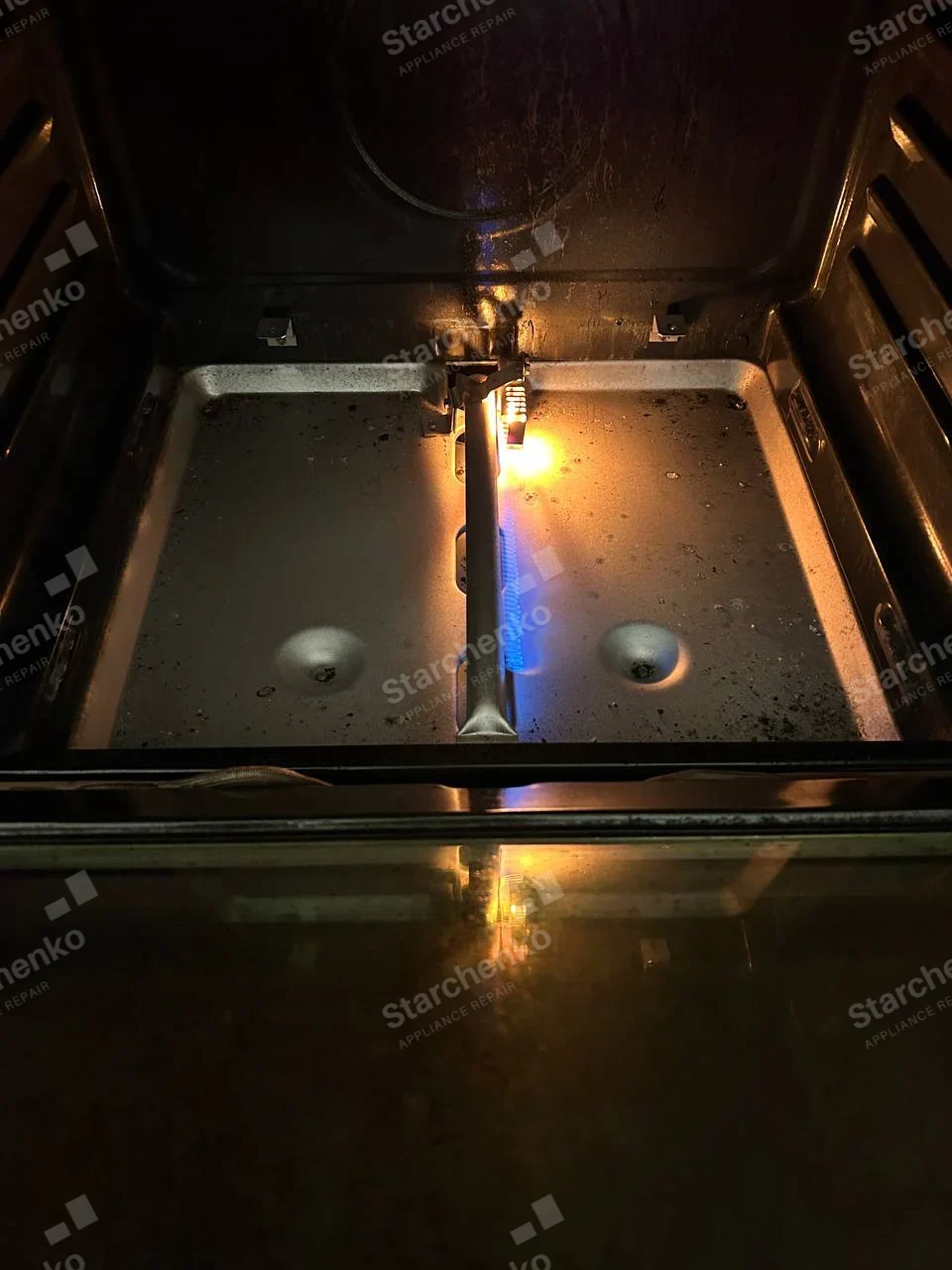 Gas oven bake burner under the removed oven floor, flame burning on one side only