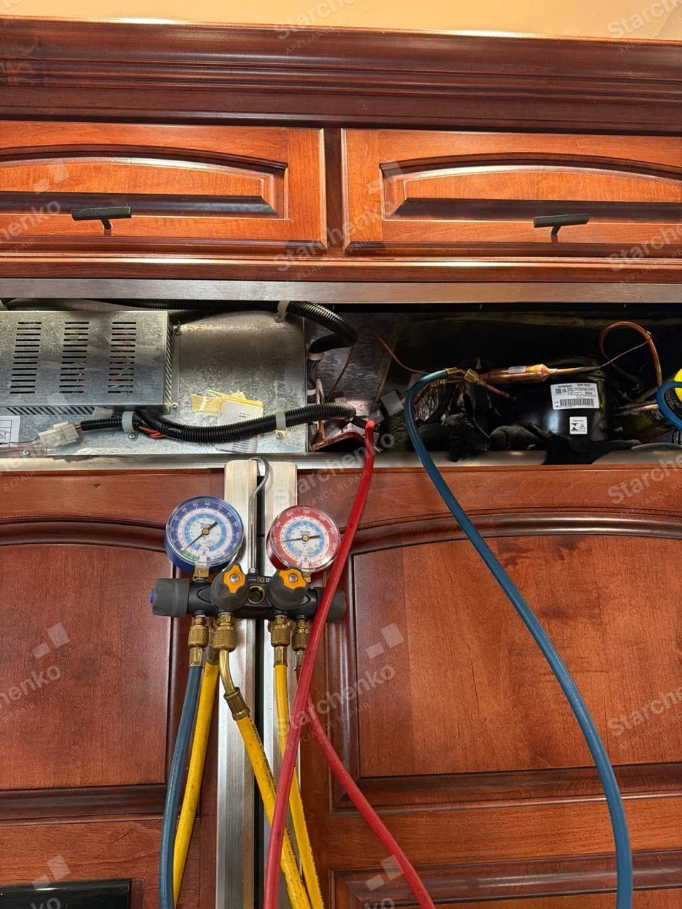 Manifold gauges connected to a panel-ready built-in refrigerator with the top grille removed over the compressor