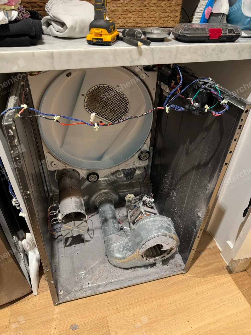 Dryer with the front panel and drum removed, exposing a lint-covered blower housing and heater duct