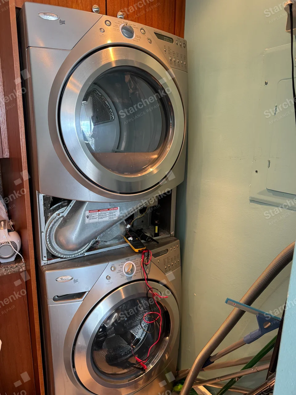 Stacked Whirlpool Duet dryer with the lower front panel removed, exposing the blower housing, and a multimeter below it