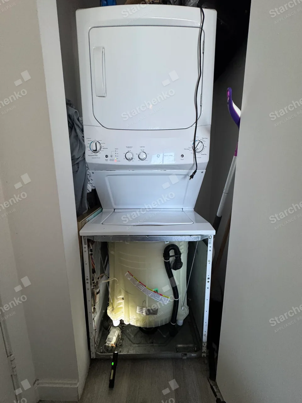 GE stacked washer and dryer with the washer front panel removed, exposing the tub and drain hose
