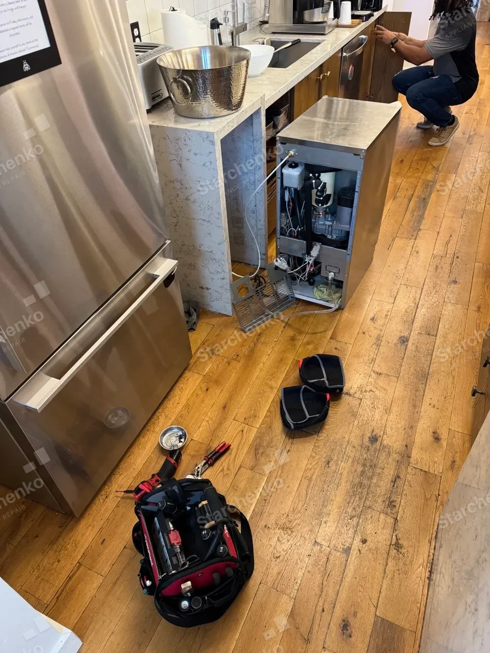 Stainless U-Line under-counter wine cooler pulled onto the floor beside a tool bag