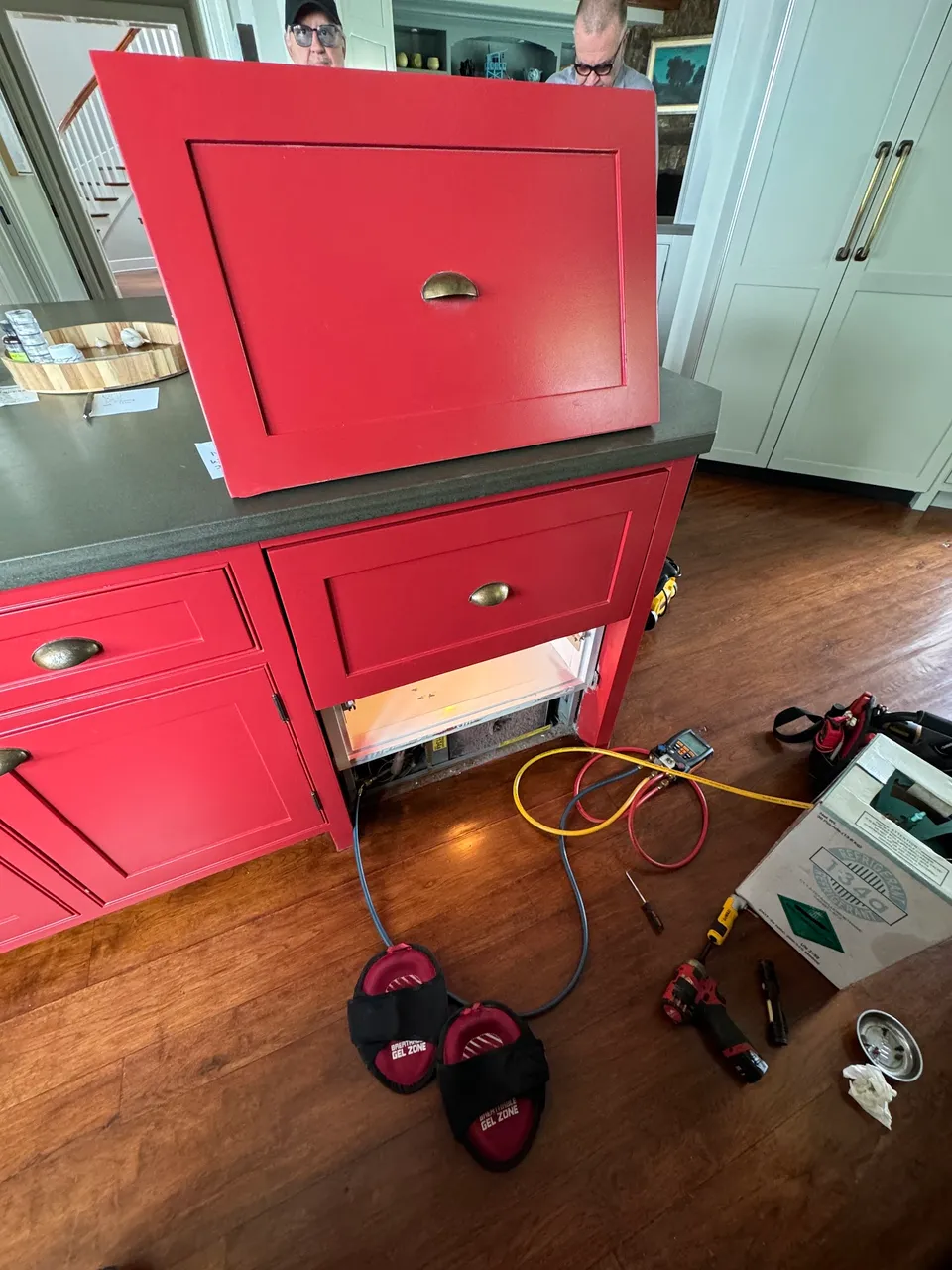 Built-in refrigerator drawer opened in red cabinetry with gauges and a refrigerant cylinder on the floor